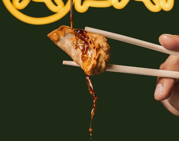 Gyoza doré tenu aux baguettes, sauce soja versée à la minute