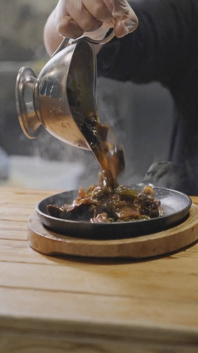 Le chef verse le bœuf sauté fumant sur la plaque en fonte